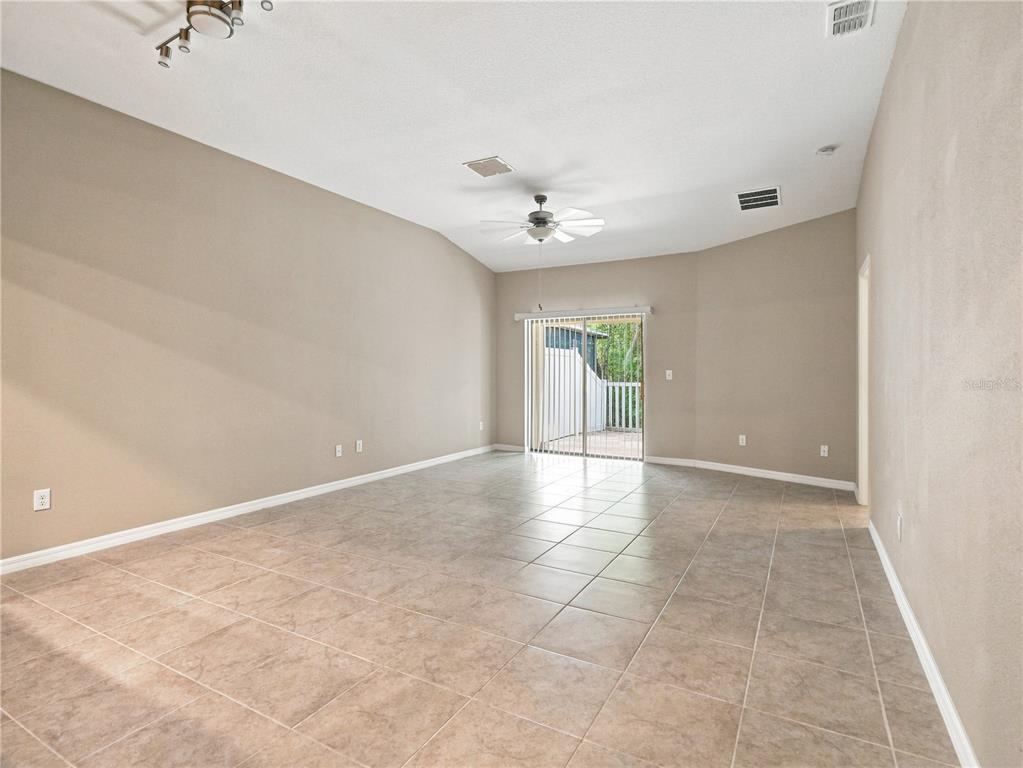 An empty living room features beige walls, tile flooring, a ceiling fan, and sliding glass doors — 13432 CREST LAKE DRIVE, HUDSON, FL