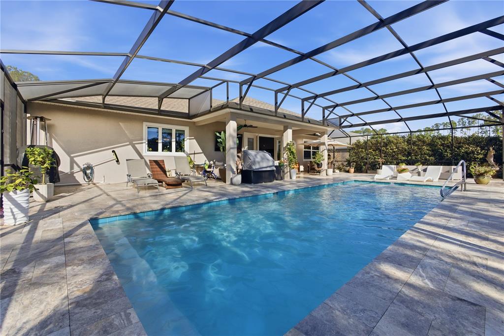 A rectangular swimming pool sits on a stone patio inside a large screened-in pool enclosure — 35 EDGELY LANE, PALM COAST, FL