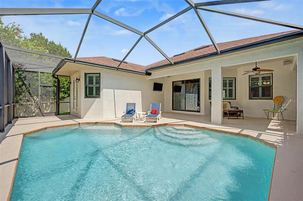 A swimming pool with a screened enclosure sits outside a house with a covered patio — 1045 MAZA PLACE, TRINITY, FL