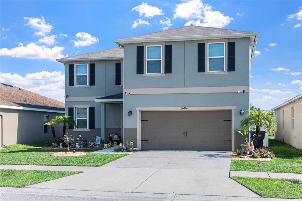 A two-story house with a light blue exterior, a brown garage door, and a concrete driveway — 10624 ALDO MORO DRIVE, WIMAUMA, FL