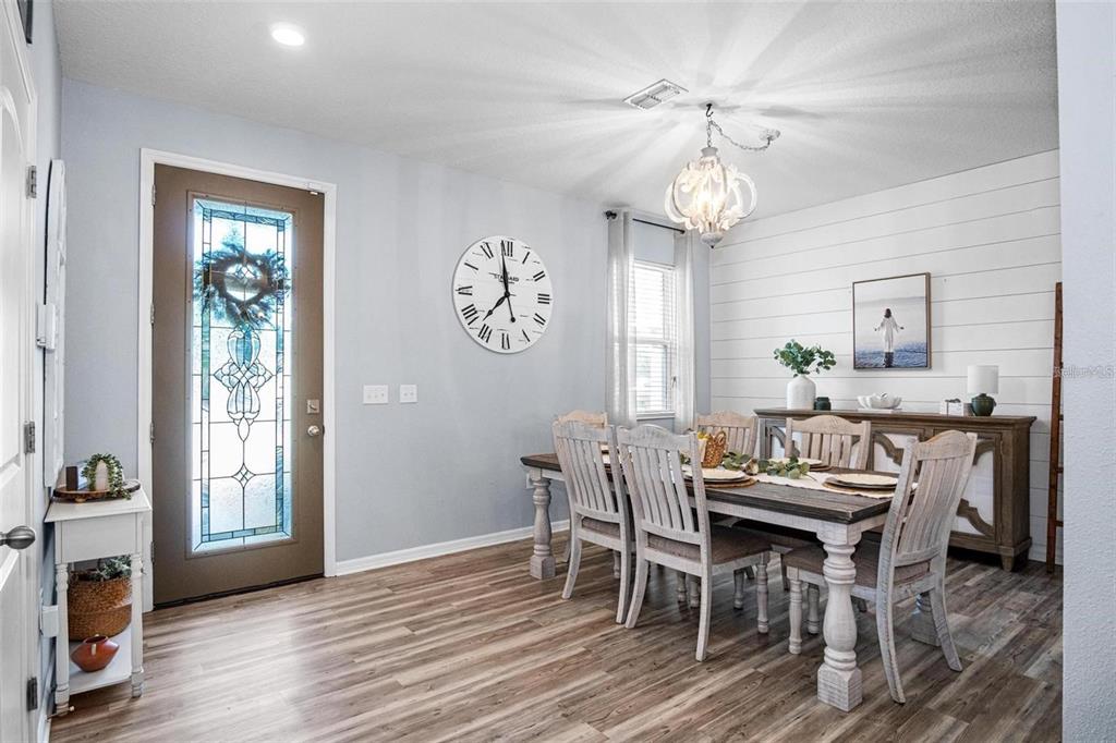 A dining room features a wooden table, white chairs, a shiplap wall, and a large clock — 10624 ALDO MORO DRIVE, WIMAUMA, FL