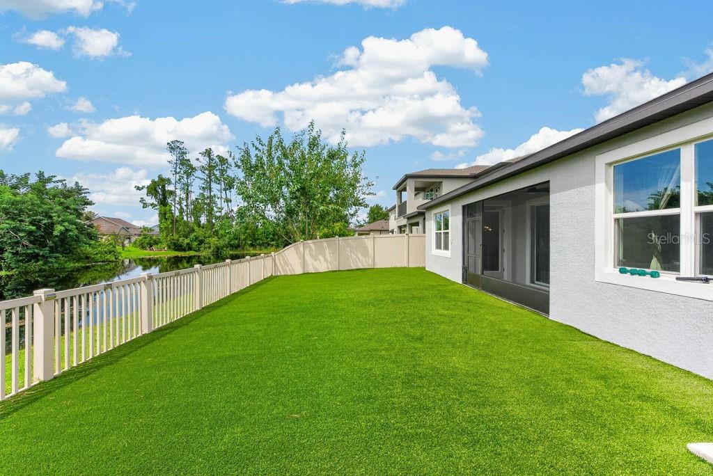 A backyard with a green lawn, a white fence, and a view of a pond — 22310 WOODMEN HALL DRIVE, LAND O LAKES, FL