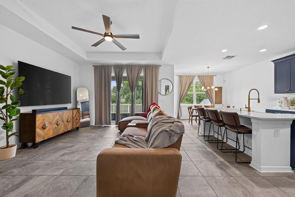 An open-concept living room and kitchen featuring tile flooring, a large television, and bar seating — 22310 WOODMEN HALL DRIVE, LAND O LAKES, FL