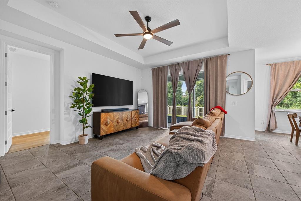 A living room features a brown leather sofa, a large television, and tile flooring — 22310 WOODMEN HALL DRIVE, LAND O LAKES, FL