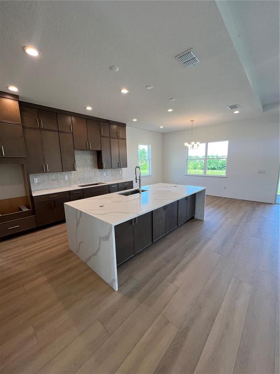 A modern kitchen features dark wood cabinetry, a large white quartz island, and light flooring — 1712 STONECLIFF DRIVE, APOPKA, FL