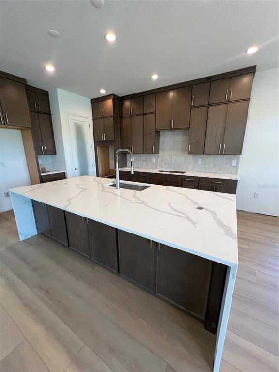 A kitchen features dark wood cabinets, a large white quartz island, and light wood flooring — 1712 STONECLIFF DRIVE, APOPKA, FL