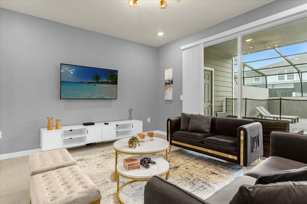 A living room features a wall-mounted television, white media console, dark sofas, and a patio — 4318 LANA AVENUE, DAVENPORT, FL
