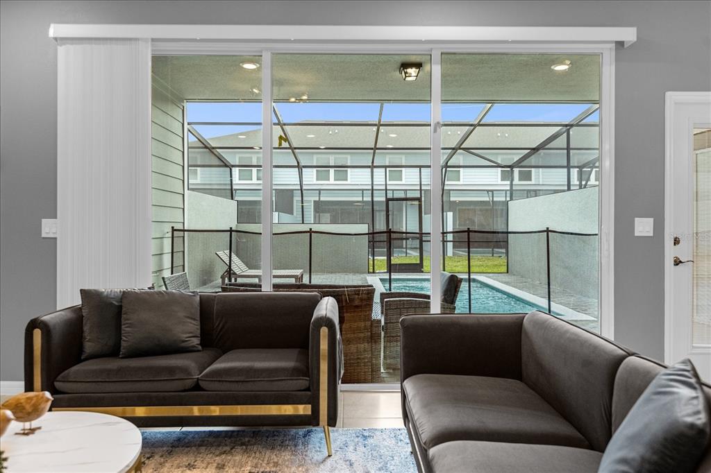 A living room with dark sofas overlooks a screened-in patio with a small swimming pool — 4318 LANA AVENUE, DAVENPORT, FL