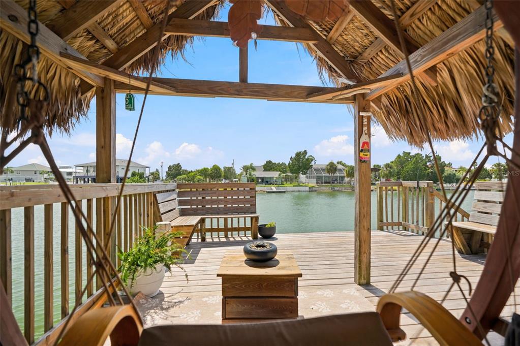 A wooden tiki hut deck overlooks a canal with built-in seating and a small table — 3199 AZALEA DRIVE, HERNANDO BEACH, FL