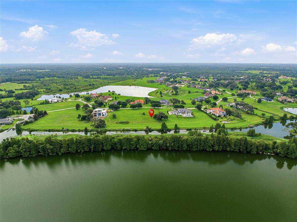 An aerial view shows a large, grassy residential lot marked with a red pin near water — 10734 OSPREY LANDING WAY, THONOTOSASSA, FL