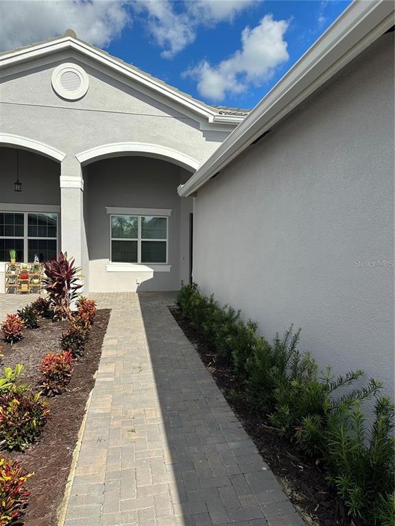 A paved walkway leads to the entrance of a house with light gray stucco walls — 4950 SIENNA ISLES AVENUE, WIMAUMA, FL