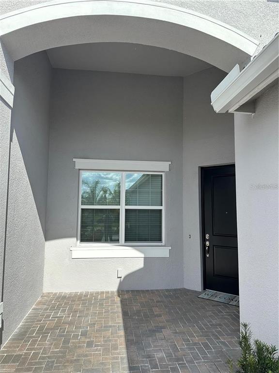 A covered entryway features a brick-paver floor, a large window, and a black front door — 4950 SIENNA ISLES AVENUE, WIMAUMA, FL