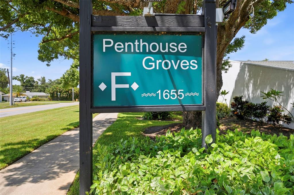 A green sign for Penthouse Groves stands on a wooden post near a sidewalk — 1655 S HIGHLAND AVENUE UNIT F133, CLEARWATER, FL