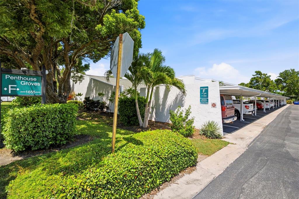 An exterior view of a residential building with covered parking and a sign for Penthouse Groves — 1655 S HIGHLAND AVENUE UNIT F133, CLEARWATER, FL