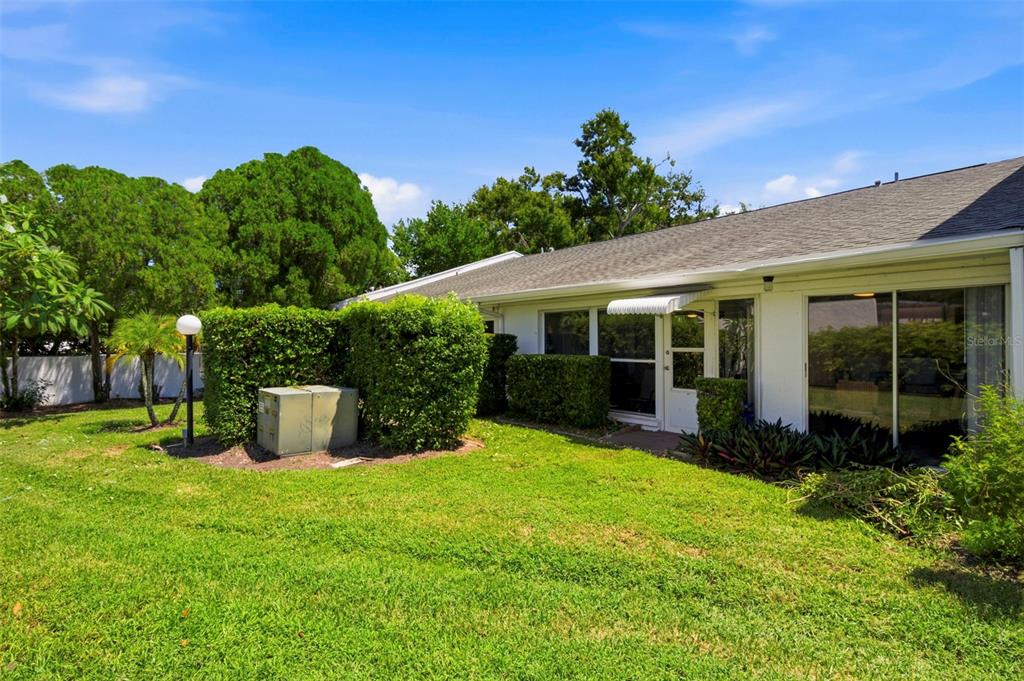 A view of a house exterior with a green lawn, landscaping, and a sliding glass door — 1655 S HIGHLAND AVENUE UNIT F133, CLEARWATER, FL