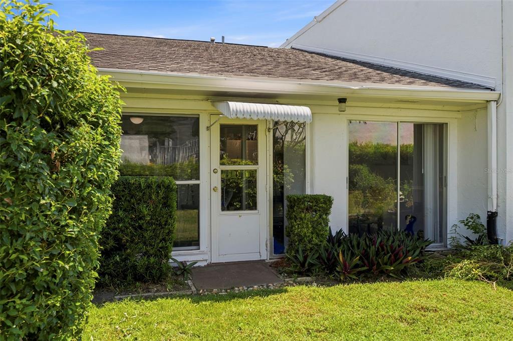 A white exterior wall features a central door with an awning and flanking sliding glass doors — 1655 S HIGHLAND AVENUE UNIT F133, CLEARWATER, FL