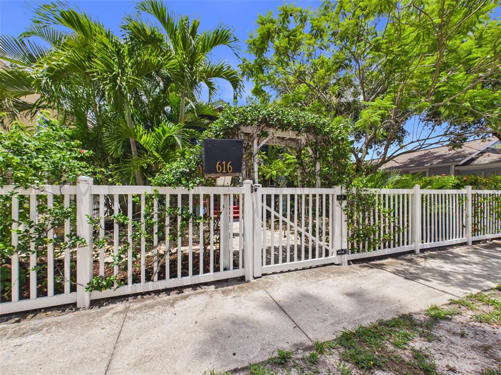 A white picket fence with a gate and an arbor stands before a lush garden — 616 15TH STREET N, ST PETERSBURG, FL