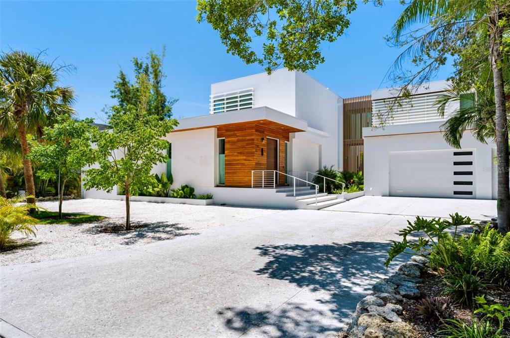 A modern white house features wood paneling at the entrance, a garage, and landscaped grounds — 1355 ROBERTS BAY LANE, SARASOTA, FL