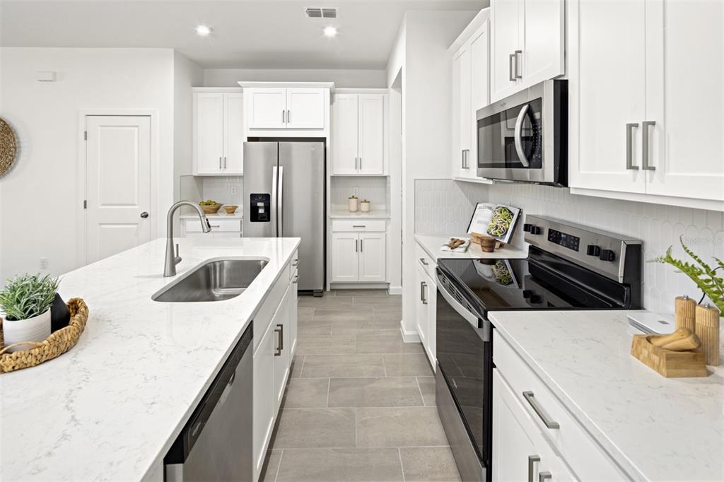 A modern kitchen features white cabinets, stainless steel appliances, and a large quartz-topped island — 13471 GOOD VIBES AVENUE, ORLANDO, FL