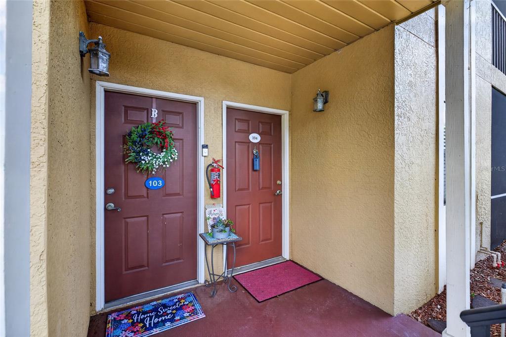 Two brown apartment doors with unit numbers 103 and 104 on a covered exterior porch — 10125 SAILWINDS BOULEVARD N UNIT 104, LARGO, FL
