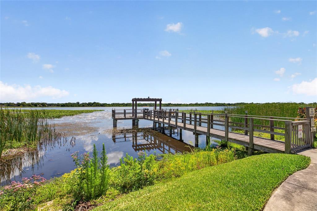 A wooden pier with a pergola extends into a lake surrounded by tall green grasses — 10125 SAILWINDS BOULEVARD N UNIT 104, LARGO, FL