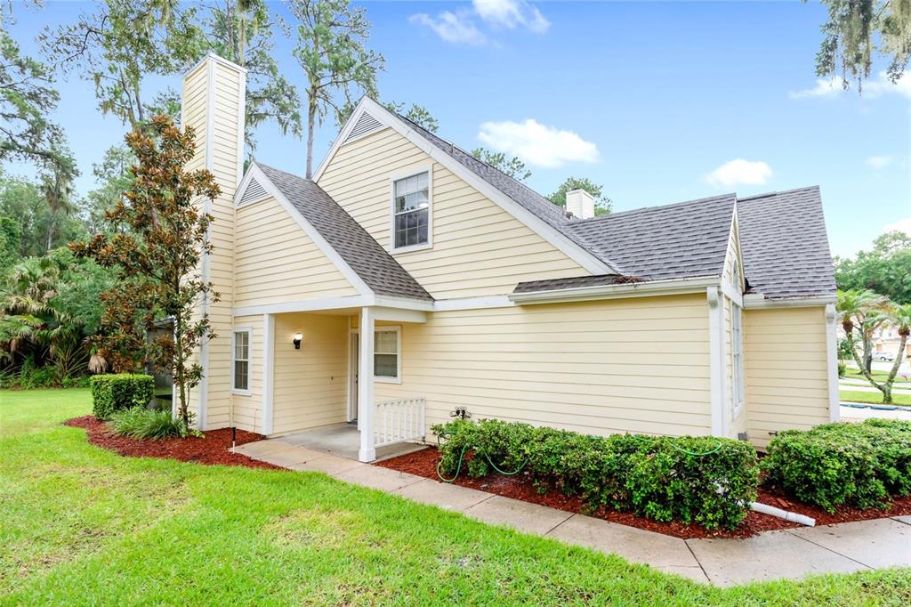 A yellow-sided house with a chimney and a covered entryway sits on a grassy lawn — 3614 PINE KNOT DRIVE UNIT 3614, VALRICO, FL