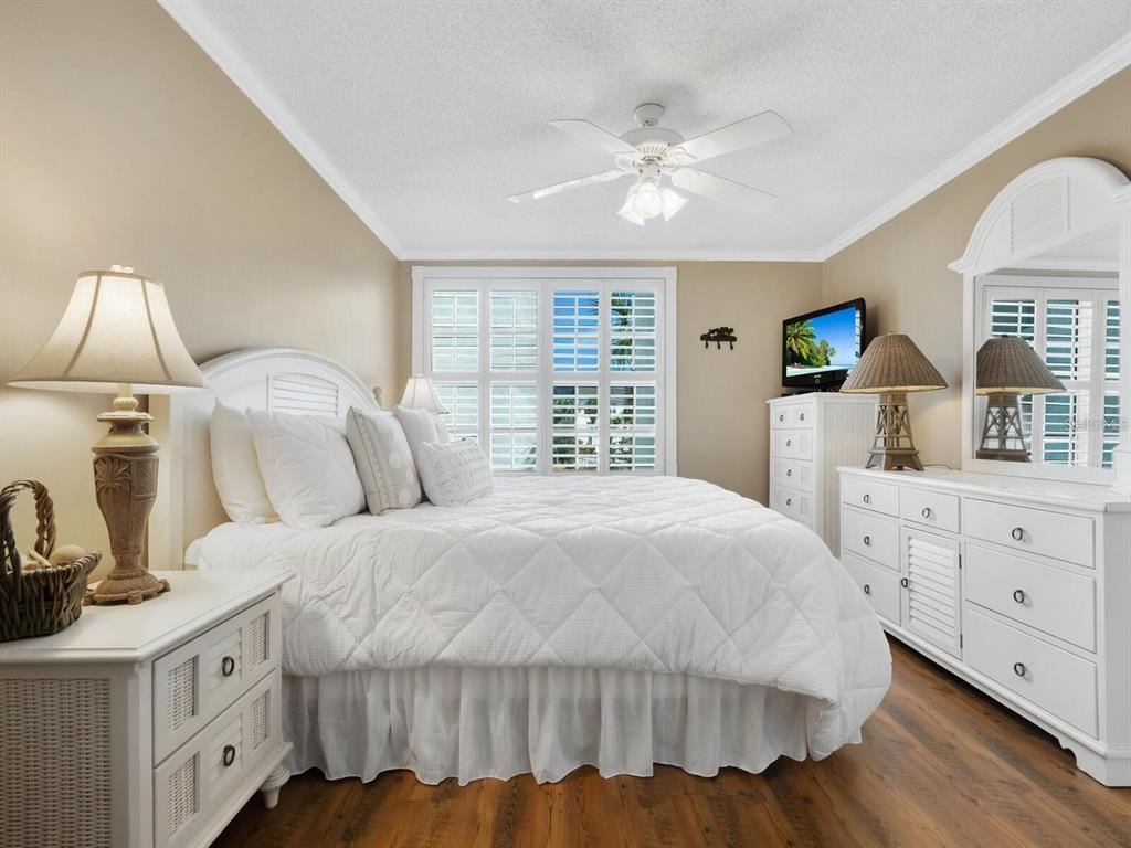 A bedroom features a white bed, matching furniture, a ceiling fan, and wood-look flooring — 600 SUTTON PLACE UNIT 201, LONGBOAT KEY, FL