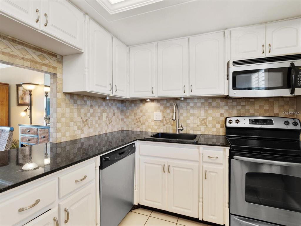 A kitchen features white cabinets, black granite countertops, a stainless steel dishwasher, and a stove — 600 SUTTON PLACE UNIT 201, LONGBOAT KEY, FL