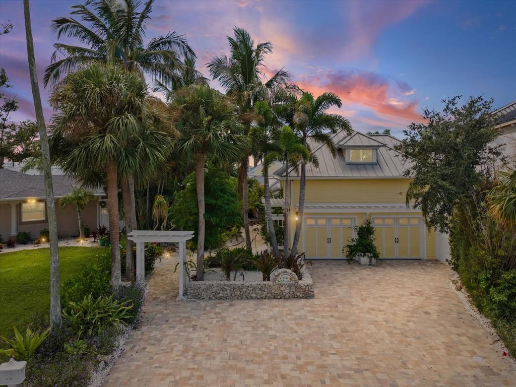 A yellow two-story house with a metal roof and a paved driveway surrounded by palm trees — 1828 VENETIAN POINT DRIVE, CLEARWATER, FL