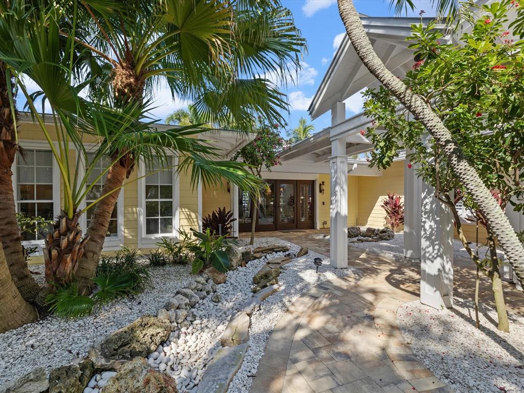 A paved walkway leads to the front entrance of a yellow house with palm trees — 1828 VENETIAN POINT DRIVE, CLEARWATER, FL