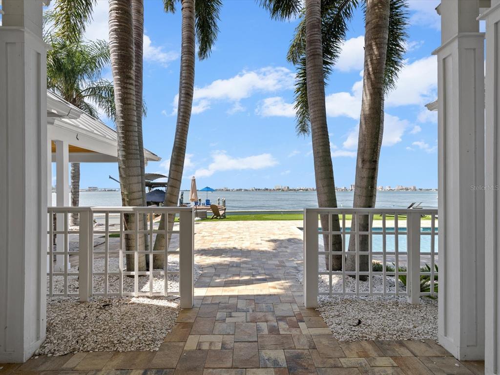 A stone patio leads through a white lattice gate toward palm trees and the water — 1828 VENETIAN POINT DRIVE, CLEARWATER, FL