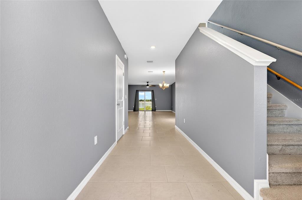 A hallway with tile flooring leads to a living area with a sliding glass door — 3809 AMBERSWEET CROSSING, PARRISH, FL