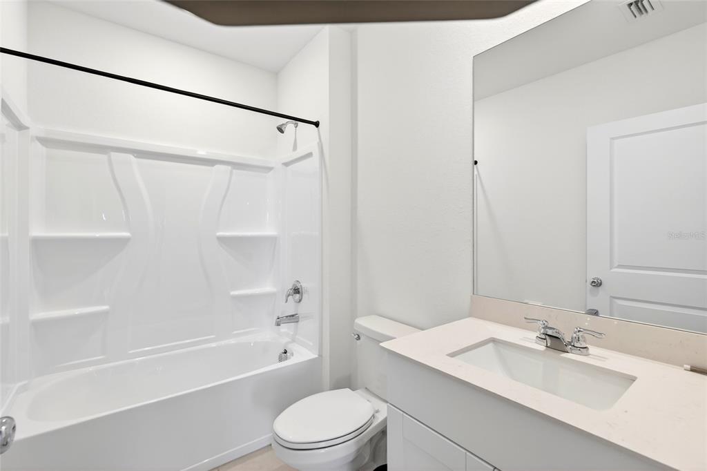 A bathroom features a white tub-shower combination, a toilet, and a vanity with a mirror — 3809 AMBERSWEET CROSSING, PARRISH, FL
