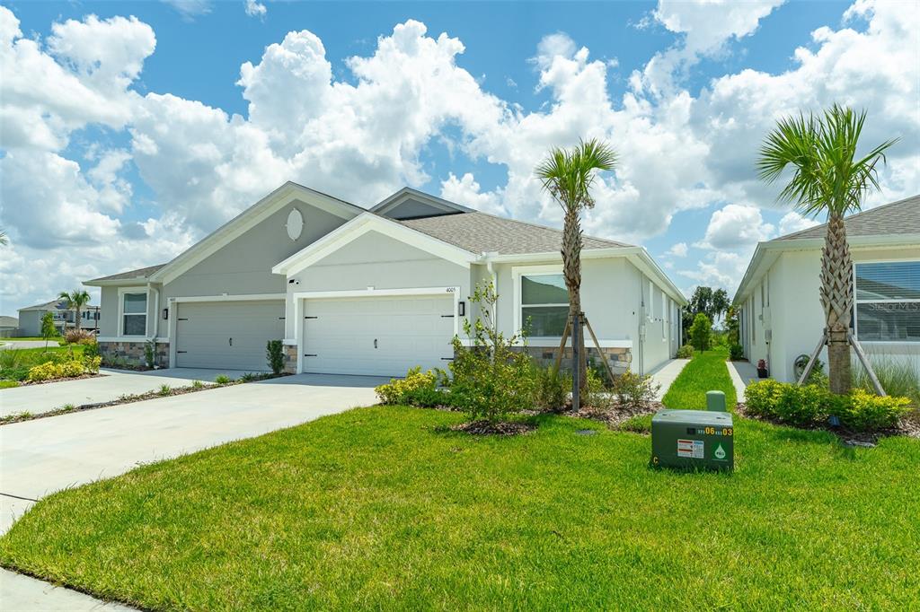 A light-colored duplex home features two garage doors, a green lawn, and two palm trees — 4005 WESTWOOD FIELDS LOOP, PLANT CITY, FL