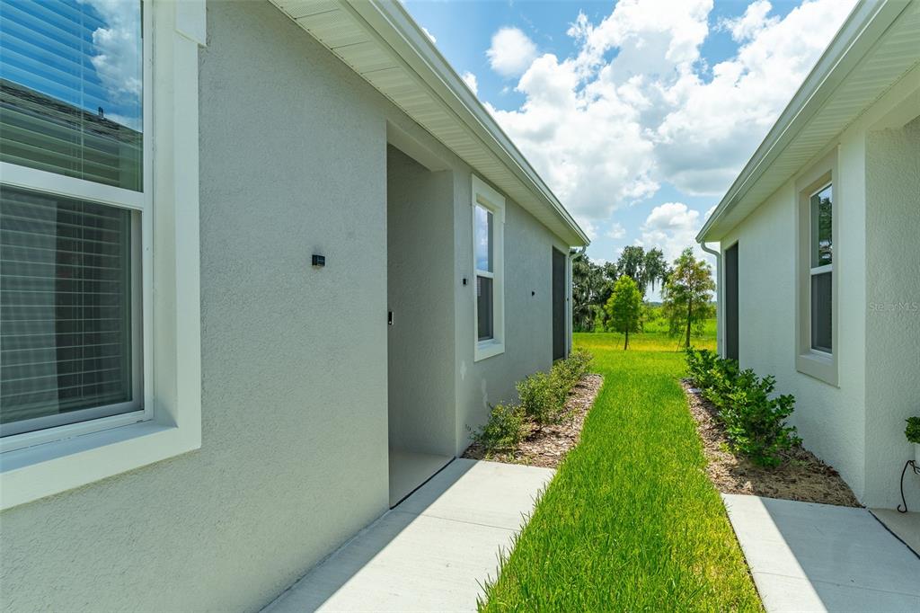 A grassy walkway separates the exterior walls of two light-colored houses under a blue sky — 4005 WESTWOOD FIELDS LOOP, PLANT CITY, FL