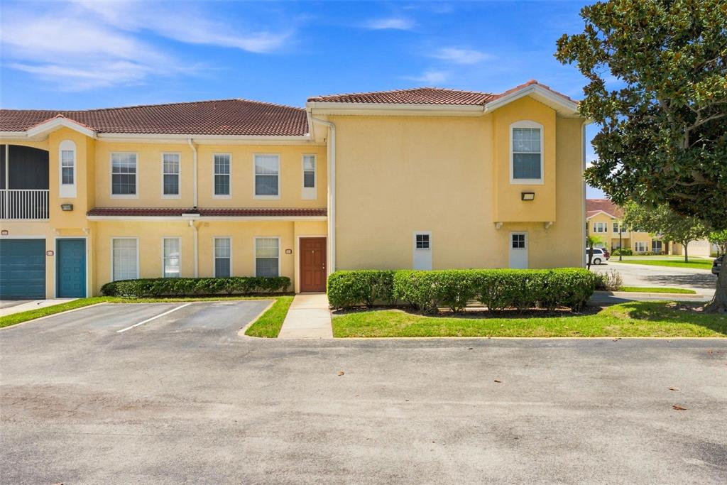 A two-story yellow stucco townhouse features a brown front door and a paved parking area — 12307 LANTANA PARK LANE UNIT 112, ORLANDO, FL