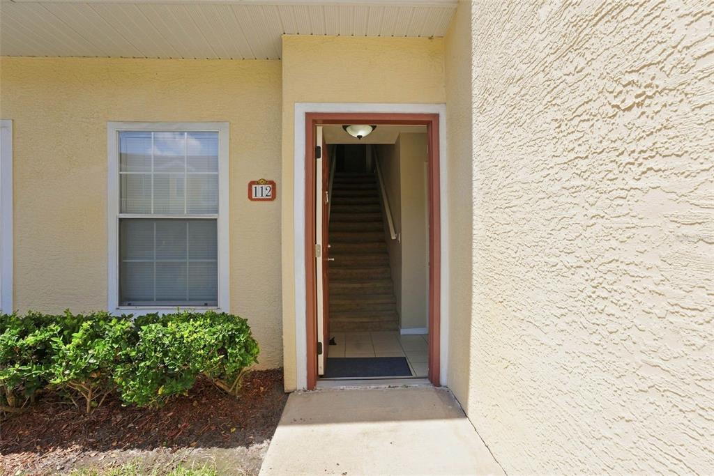 The exterior entrance of a residential unit features a beige stucco wall, a window, and stairs — 12307 LANTANA PARK LANE UNIT 112, ORLANDO, FL