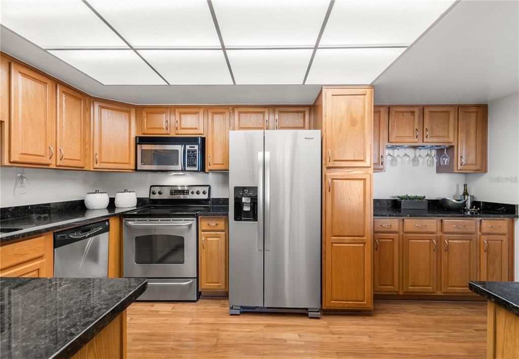 A kitchen features oak cabinets, black granite countertops, stainless steel appliances, and a drop ceiling — 400 ISLAND WAY UNIT 503, CLEARWATER BEACH, FL