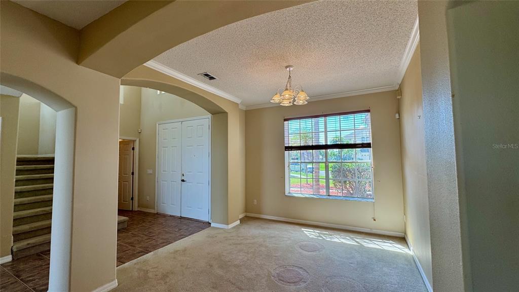 A carpeted living room features a chandelier, a large window, and an adjacent tiled entryway — 2119 PUTTER PLACE, KISSIMMEE, FL