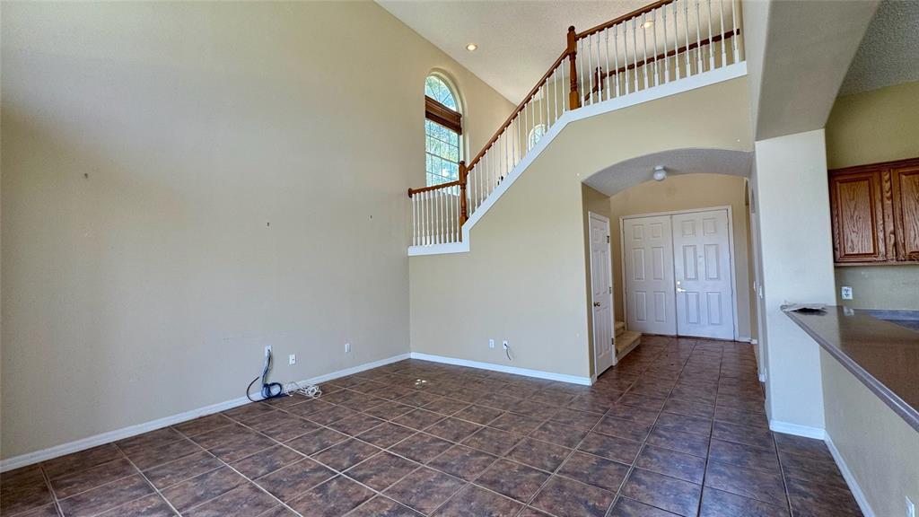 A high-ceilinged room with tile flooring, a staircase with white railings, and a front entryway — 2119 PUTTER PLACE, KISSIMMEE, FL
