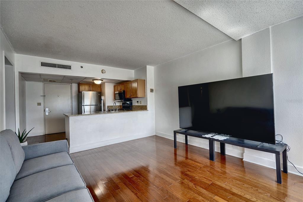 A kitchen with wood cabinets and stainless steel appliances opens into a living room area — 151 E WASHINGTON STREET UNIT 525, ORLANDO, FL