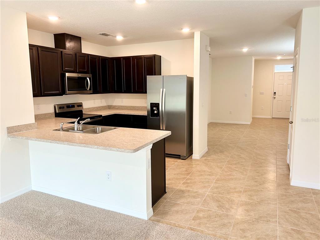 A kitchen with dark cabinets, stainless steel appliances, and a peninsula counter overlooks a tiled hallway — 3349 COSTELLO CIRCLE, WINTER HAVEN, FL