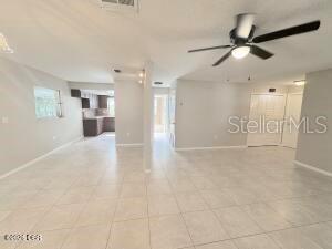 An open-concept living area with light tile flooring, a ceiling fan, and a distant kitchen — 228 COLOMBA ROAD, DEBARY, FL