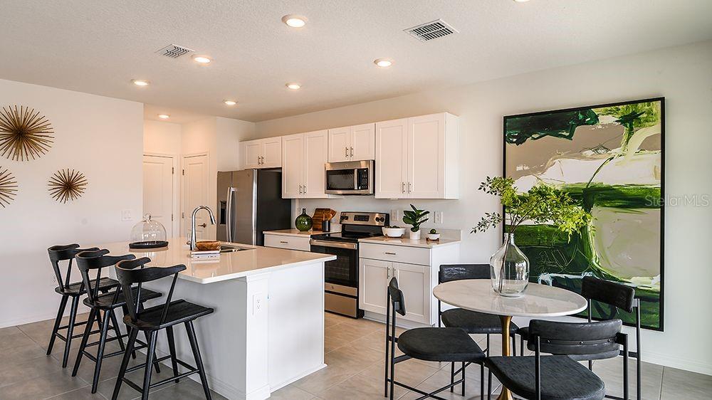 A modern kitchen features white cabinetry, a large island with bar stools, and a dining area — 6512 EQUINOX LANE, NORTH FORT MYERS, FL