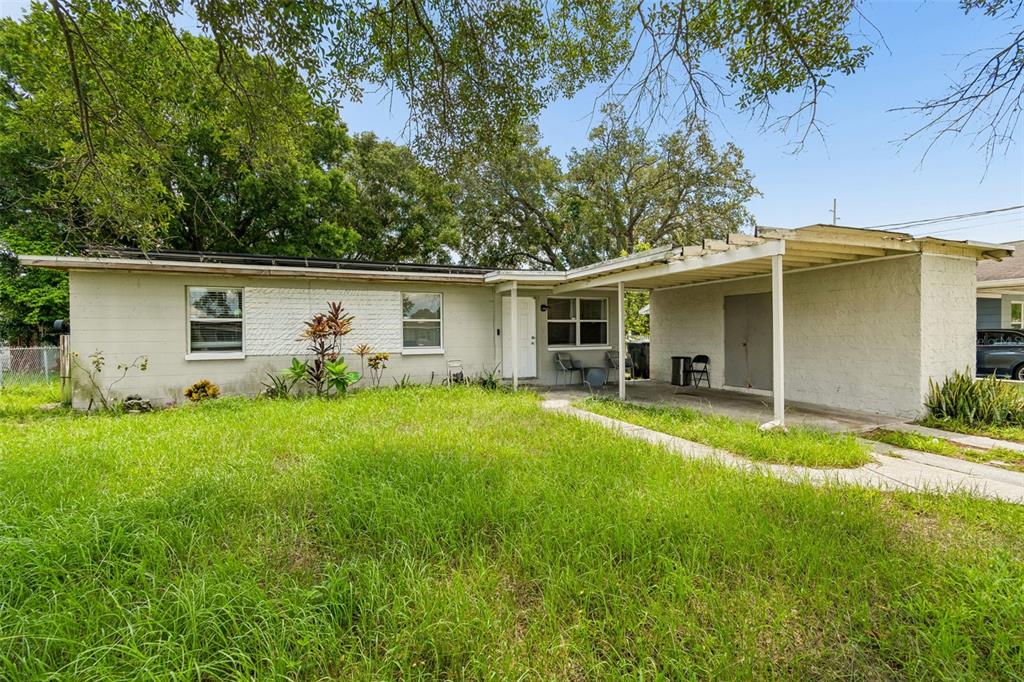 A single-story house with a white brick exterior, a front carport, and an overgrown lawn — 5020 S 86TH STREET, TAMPA, FL