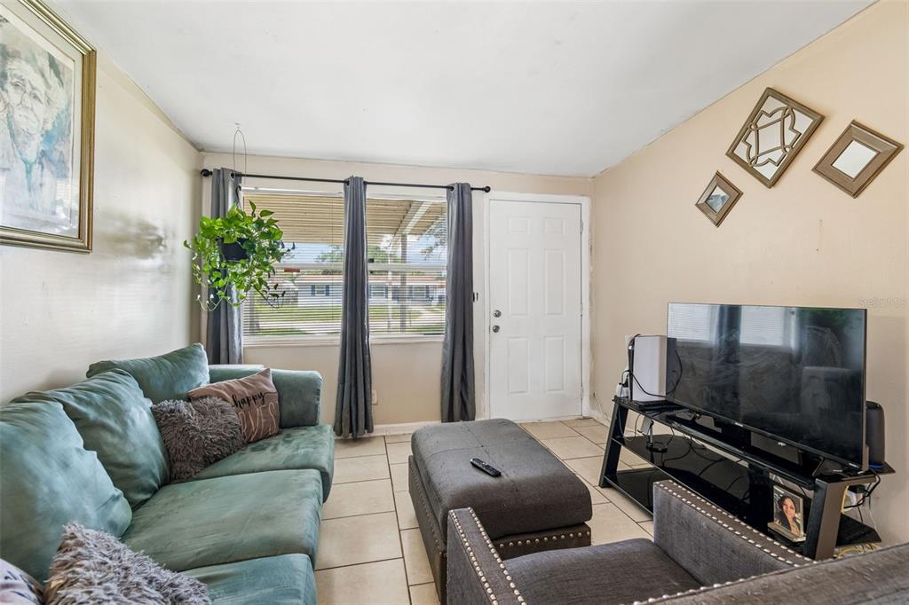 A living room features a green sofa, a grey ottoman, tile flooring, and a television — 5020 S 86TH STREET, TAMPA, FL