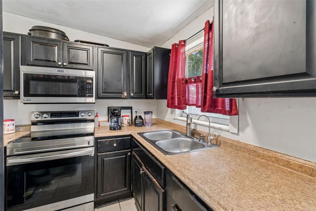 A kitchen features black cabinets, stainless steel appliances, a double sink, and tan countertops — 5020 S 86TH STREET, TAMPA, FL