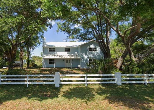 A two-story light blue house sits behind a white wooden fence under large oak trees — 916 BAYSHORE DRIVE, ENGLEWOOD, FL