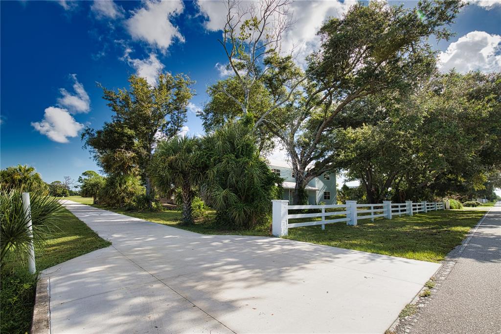 A concrete driveway leads to a house partially obscured by large trees and white fencing — 916 BAYSHORE DRIVE, ENGLEWOOD, FL