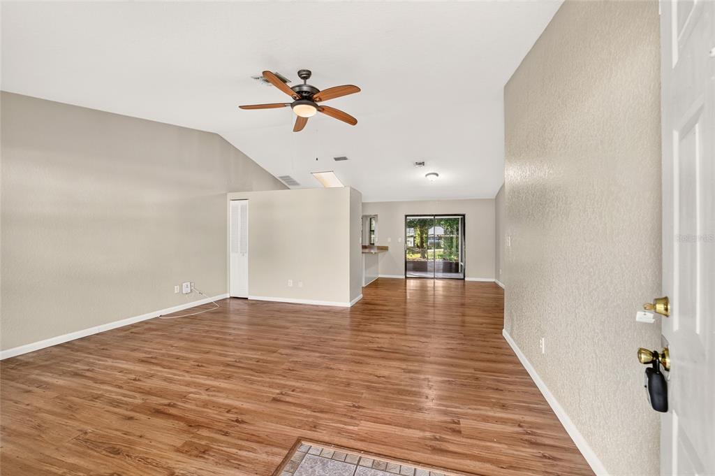 An open-concept living area features wood-look flooring, a vaulted ceiling with a fan, and sliding doors — 8 BANYAN COURSE RUN, OCALA, FL